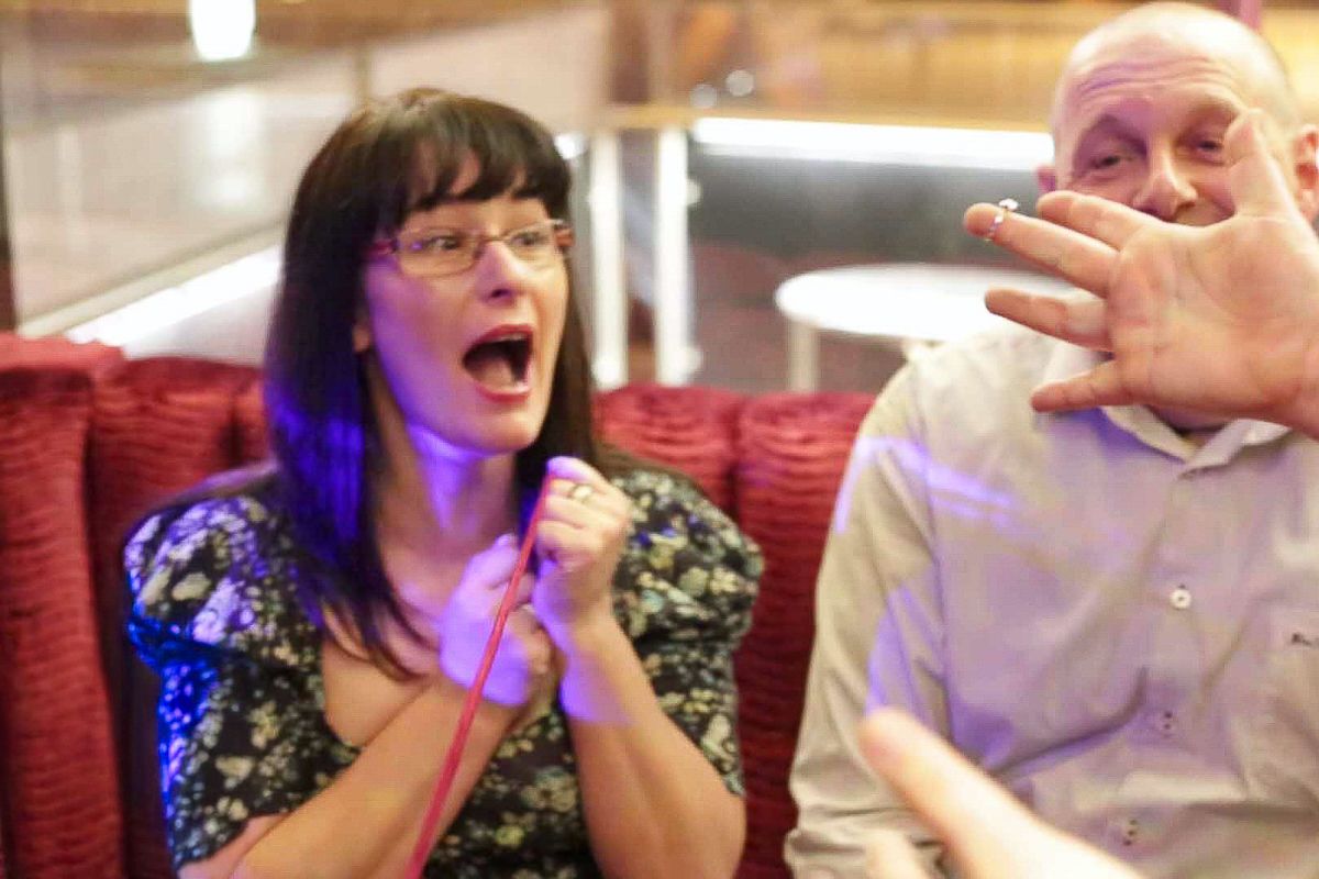 A woman reacts with shock and amazement during a magic trick performance at an indoor event.