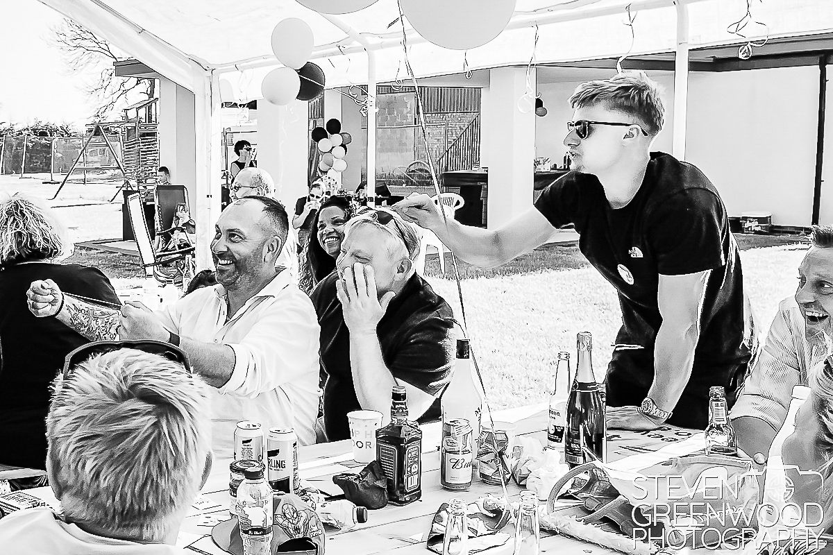 Black and white photo of guests laughing at an outdoor party under a marquee tent.