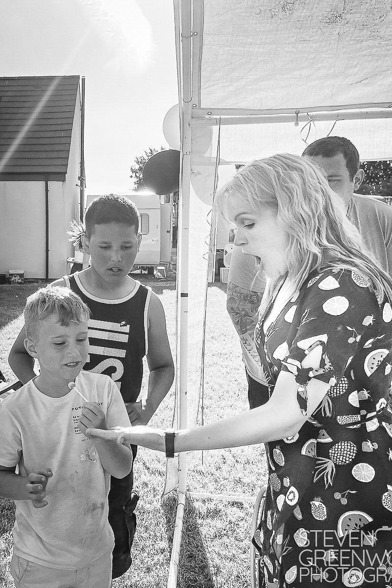 Woman in polka dot dress interacting with children at an outdoor event under a tent.
