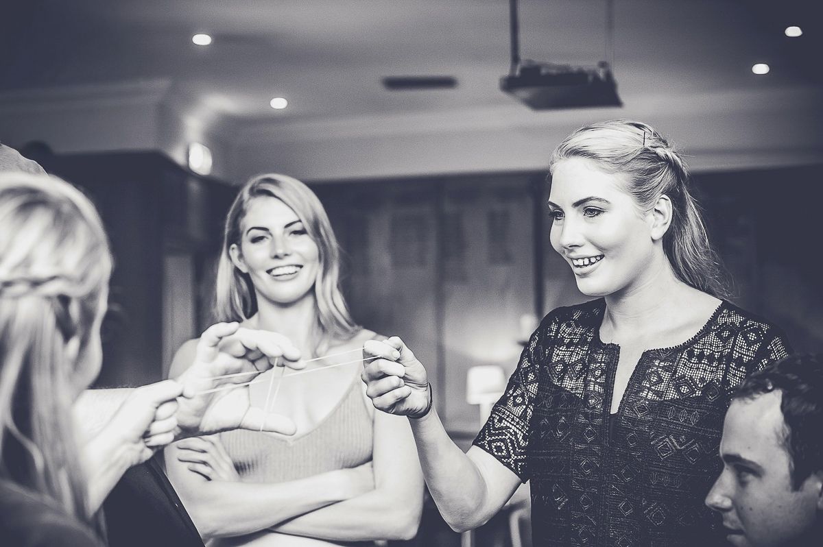 Two elegant blonde women smiling and holding hands at sophisticated indoor event in monochrome.