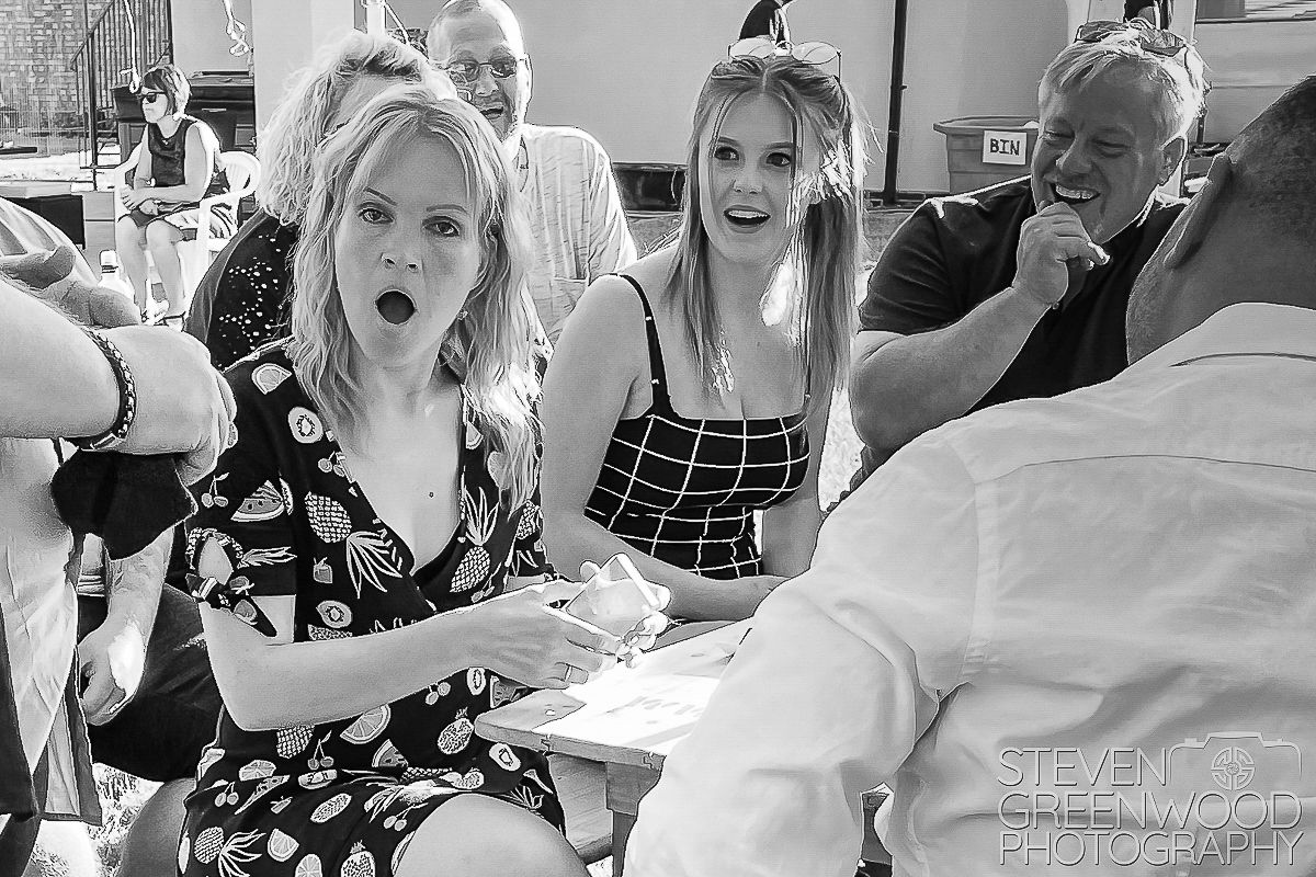 Surprised wedding guests react with excitement at reception table in black and white photo.