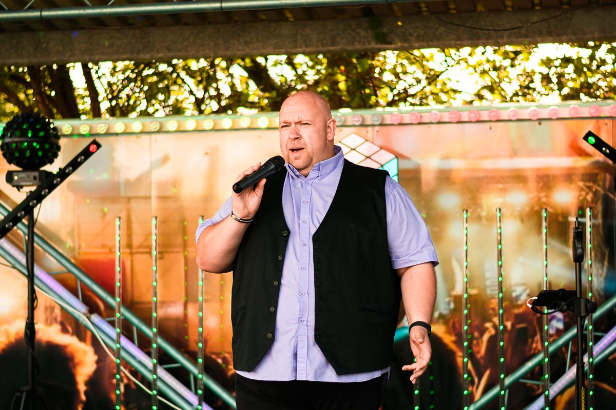 A performer singing passionately on stage with colorful stage lighting and equipment visible in the background.