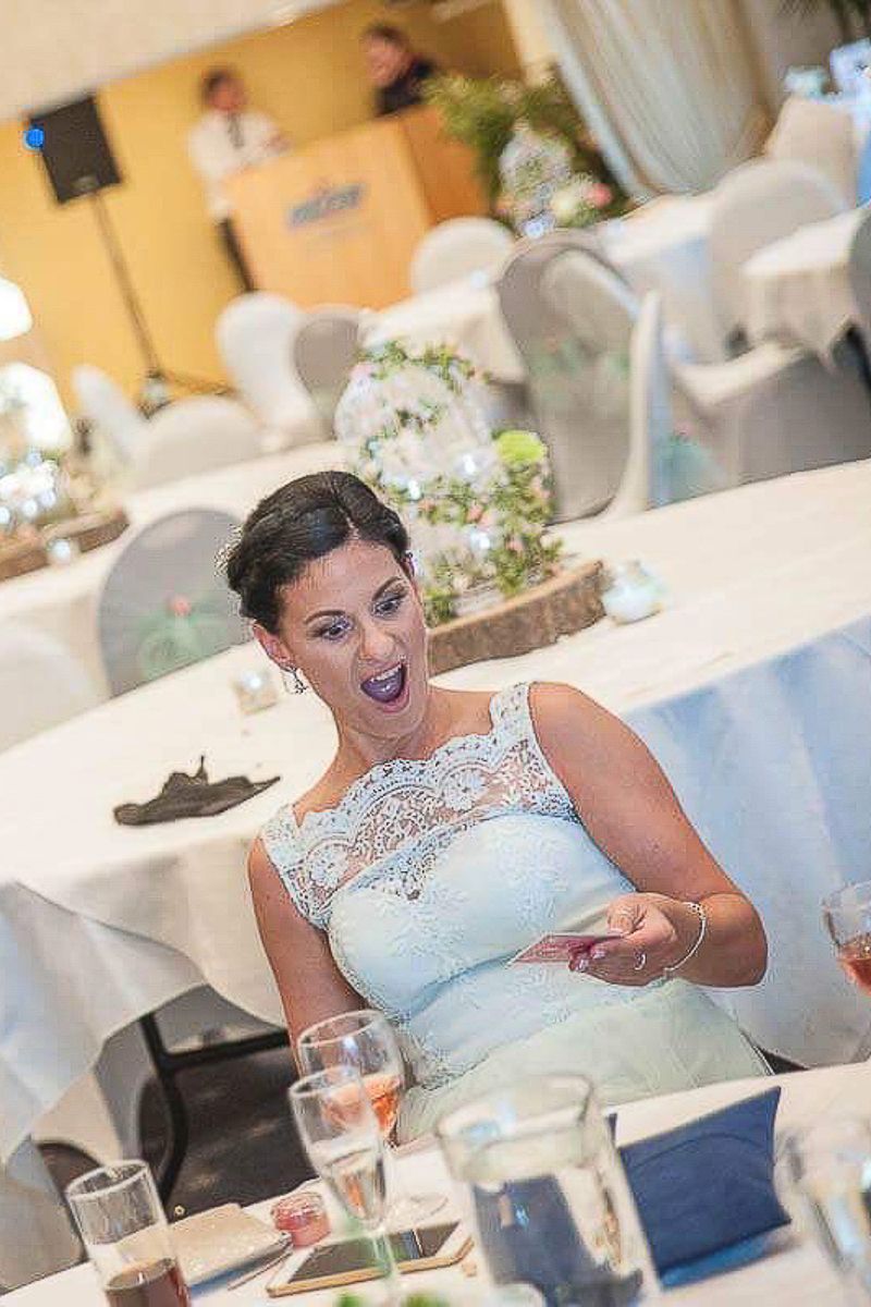 A woman in a lace dress reacts with surprise during a magician performance at a wedding reception.