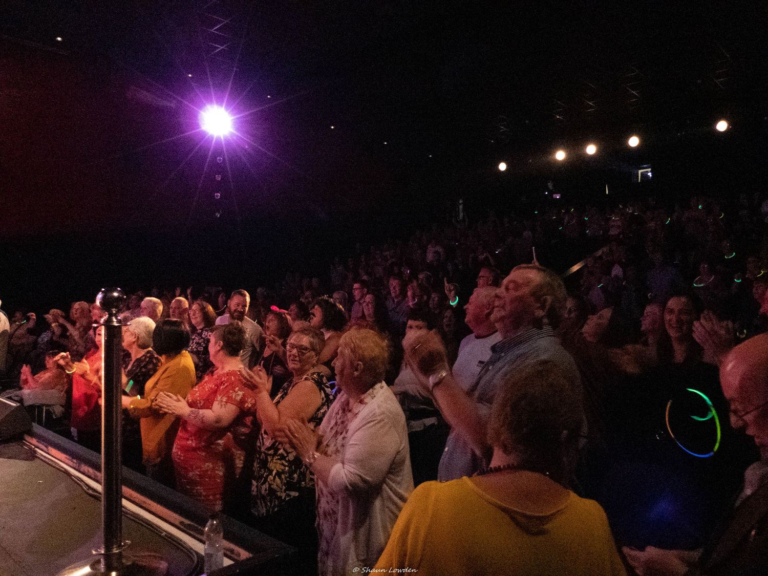 Concert audience illuminated by bright purple stage lights during a live performance.