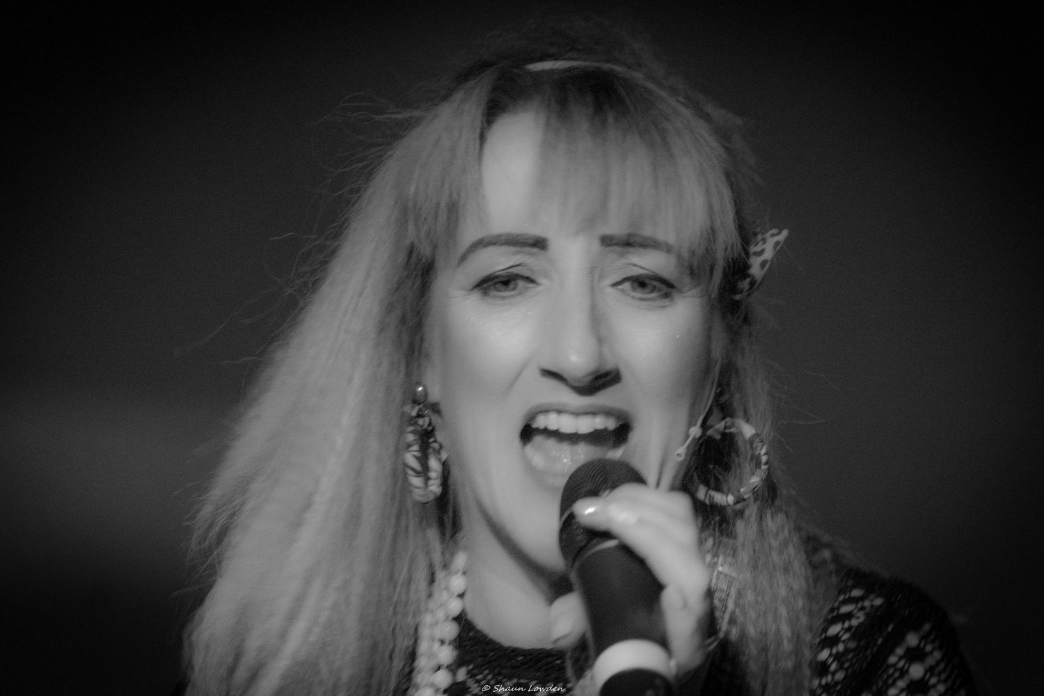 Black and white portrait of performer singing with microphone on stage.