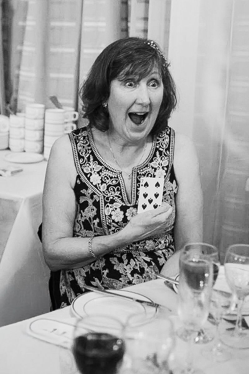 A woman reacting with surprise while holding playing cards at a wedding reception table.