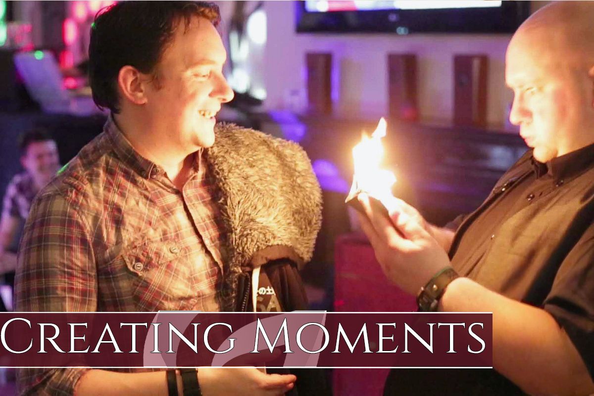 Magician performing close-up tricks with cards in a dimly lit venue creating magical moments for an engaged audience.