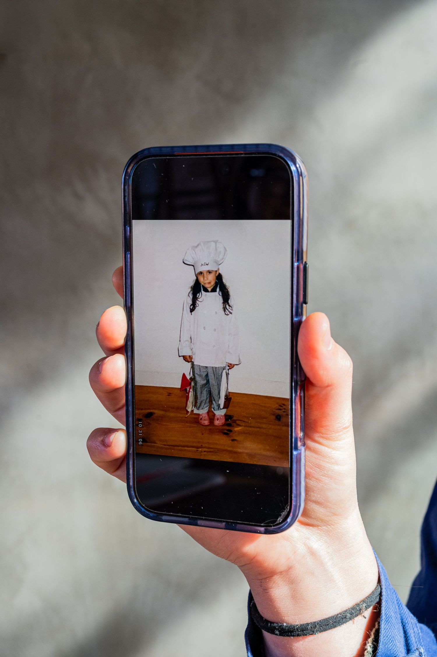 Hand holding a smartphone displaying a vintage photo of a child dressed in a white chef costume with hat.