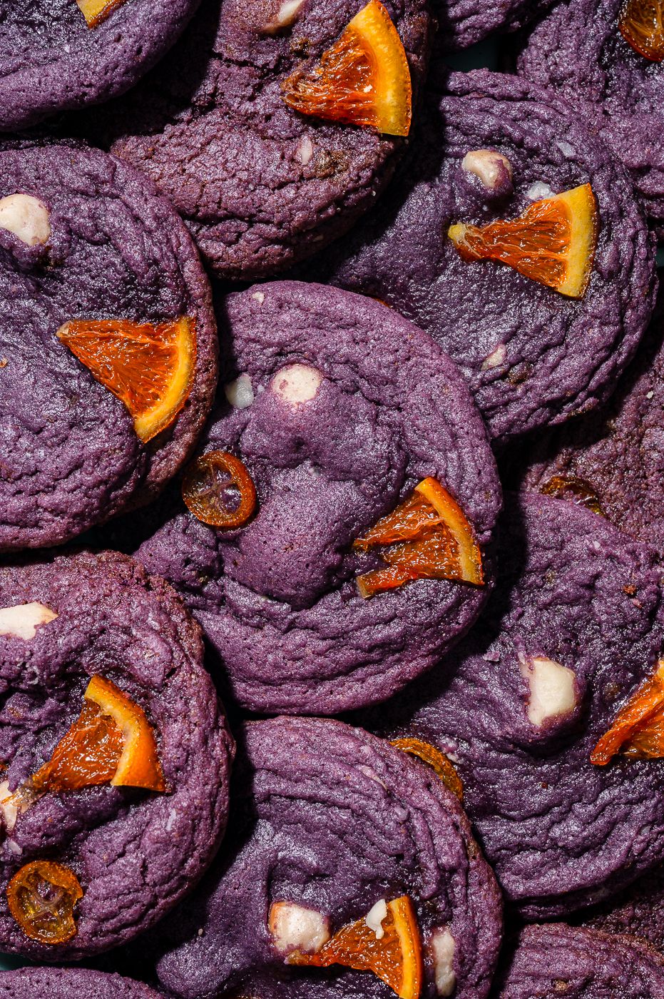 Overhead view of purple cookies with white chocolate chips and blood orange slices on dark background.