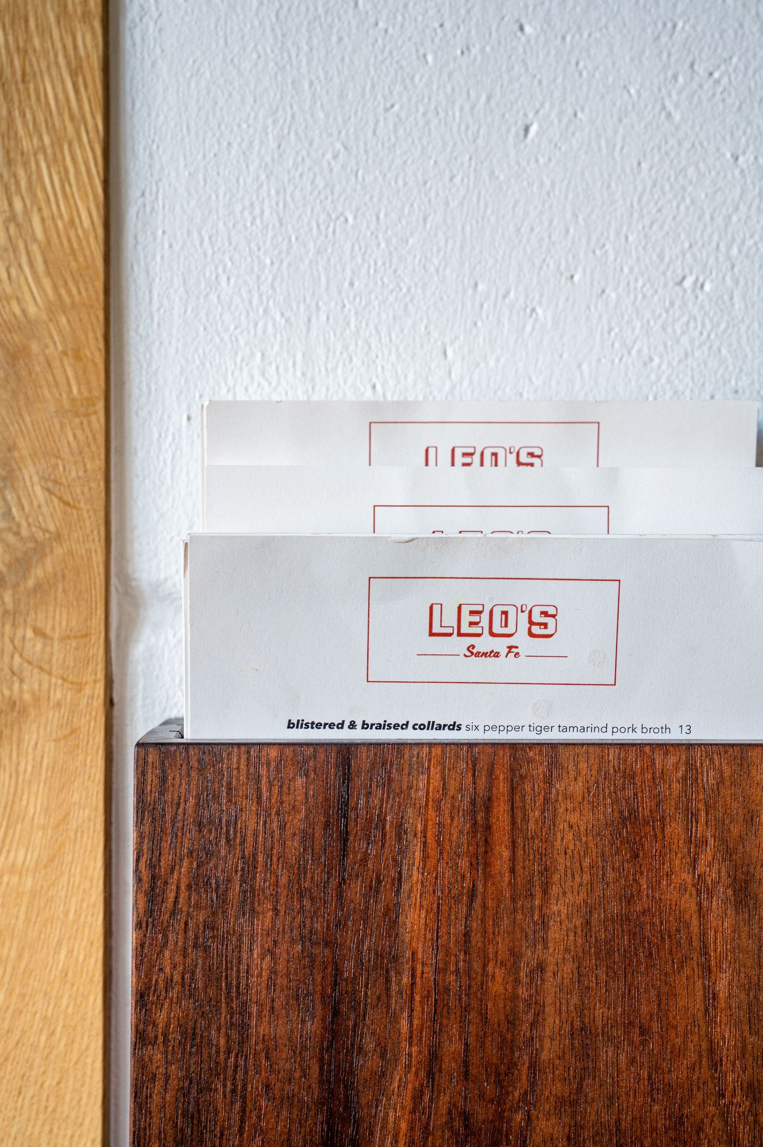 Menus for Leo's Santa Fe restaurant displayed in a wooden holder against a white wall.