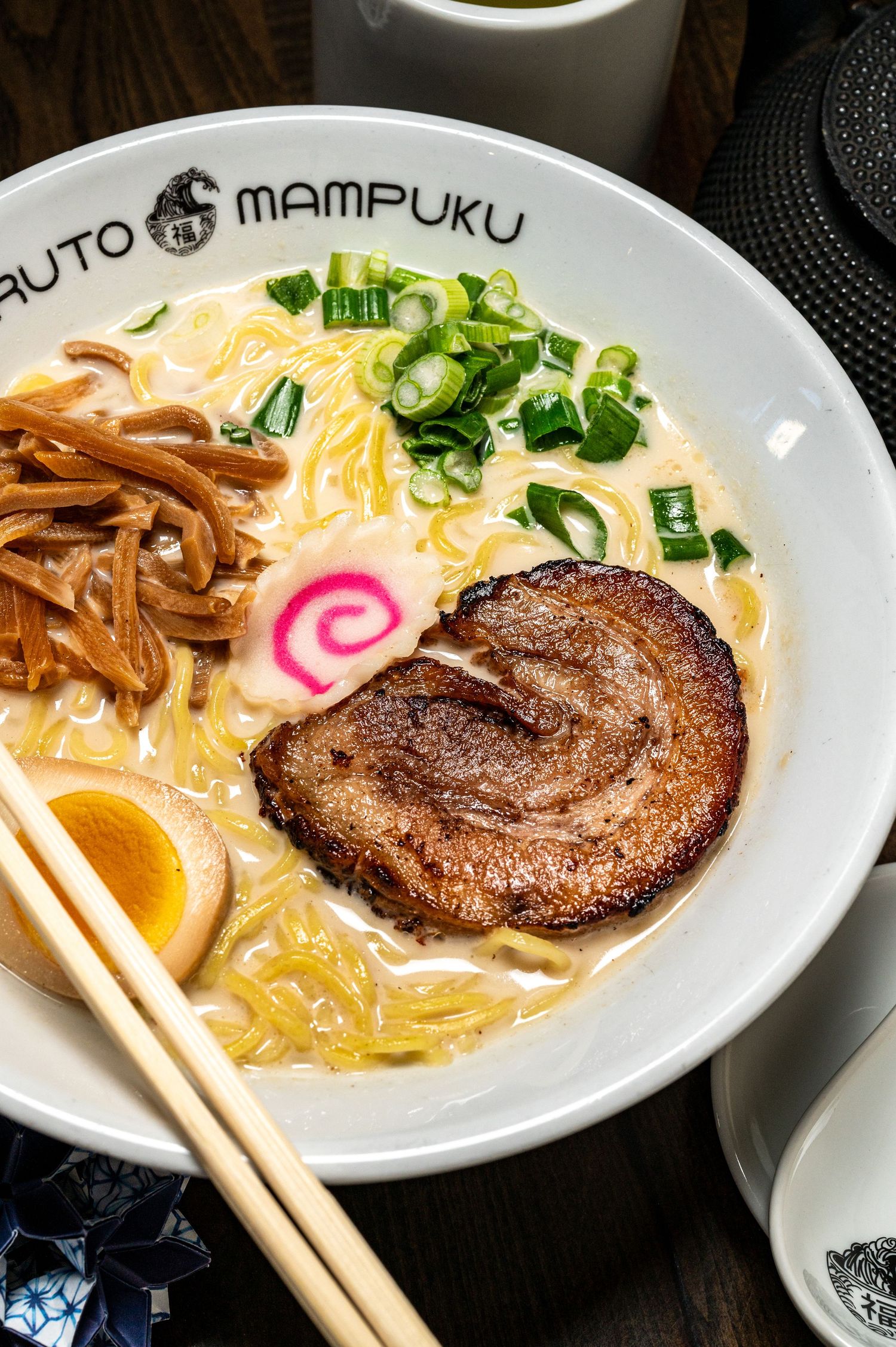 A bowl of creamy tonkotsu ramen with chashu pork, soft-boiled egg, green onions, and narutomaki at Mampuku.