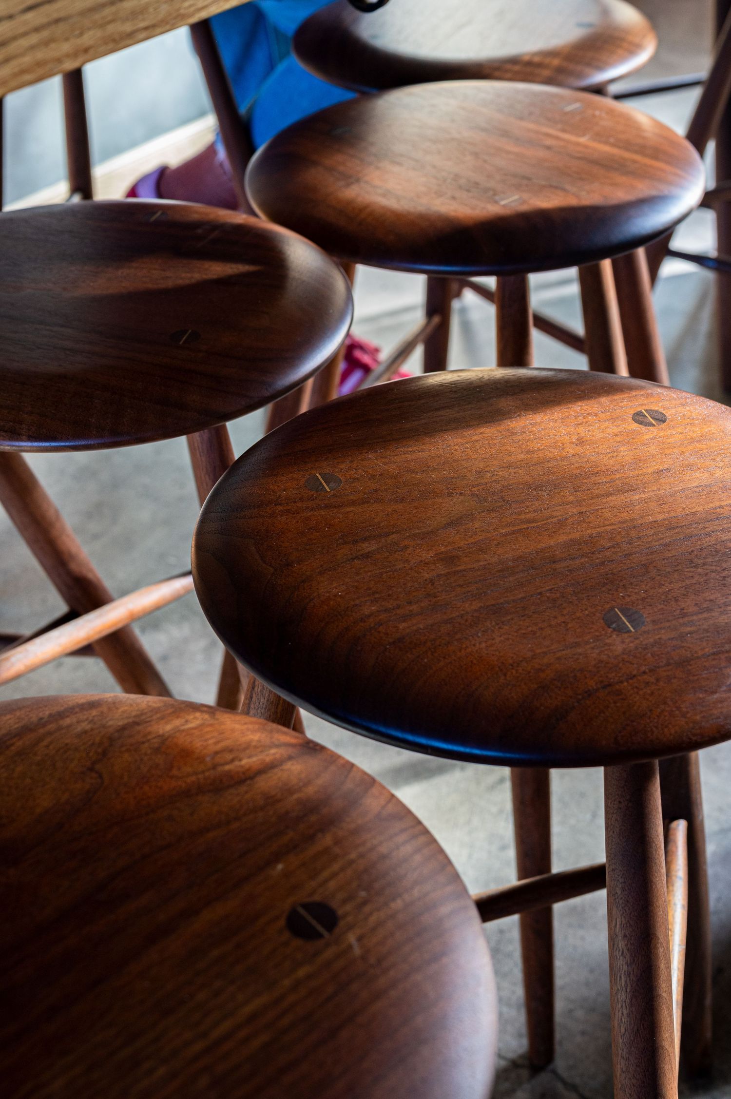 Row of round wooden bar stools with warm brown finish arranged closely together in a cafe or restaurant setting.