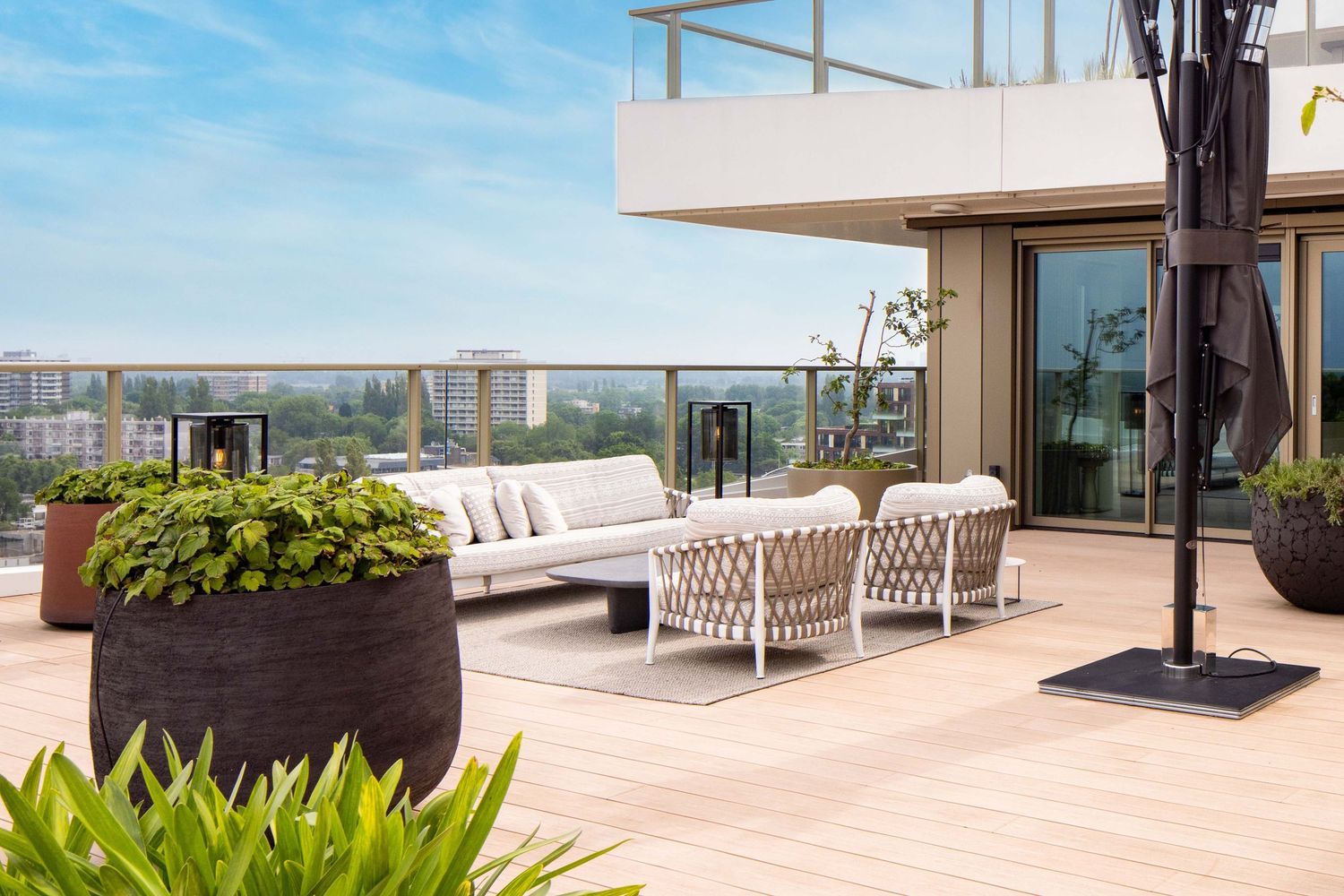 Modern outdoor terrace with glass railings and wooden decking offers panoramic views of a coastal landscape.
