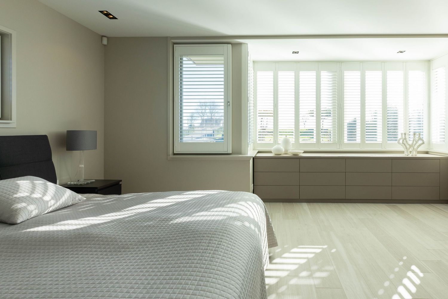 Modern bedroom interior with white bedding and built-in window bench seating offering natural light and storage.