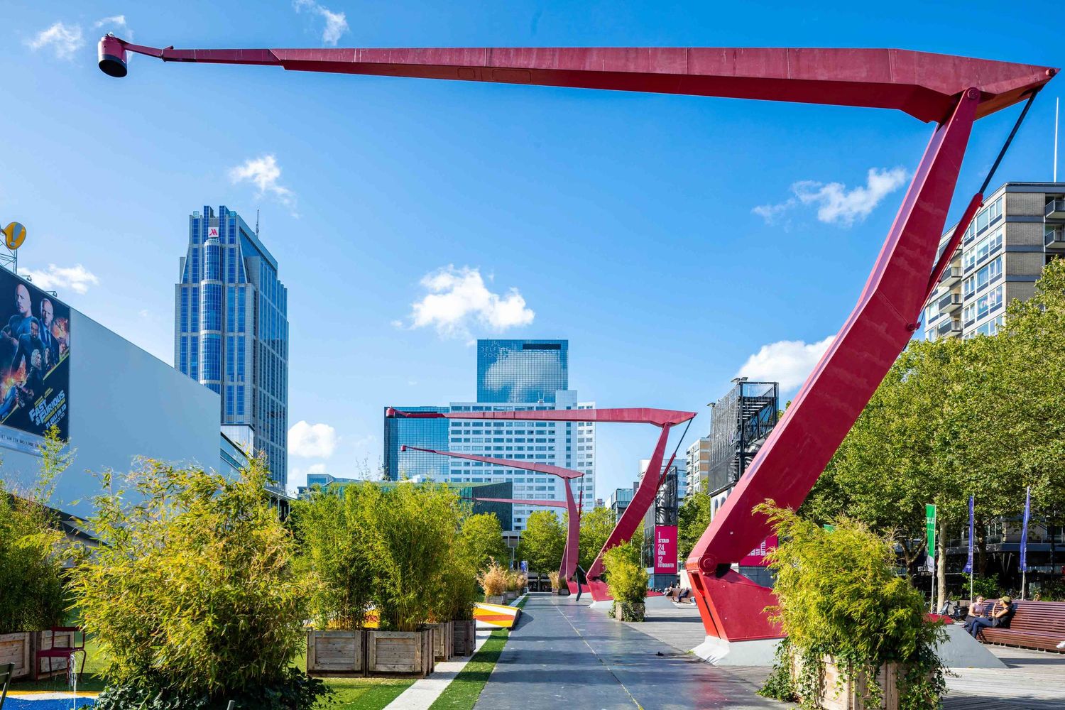 A bright red architectural sculpture curves across the sky against modern buildings and trees in an urban setting.