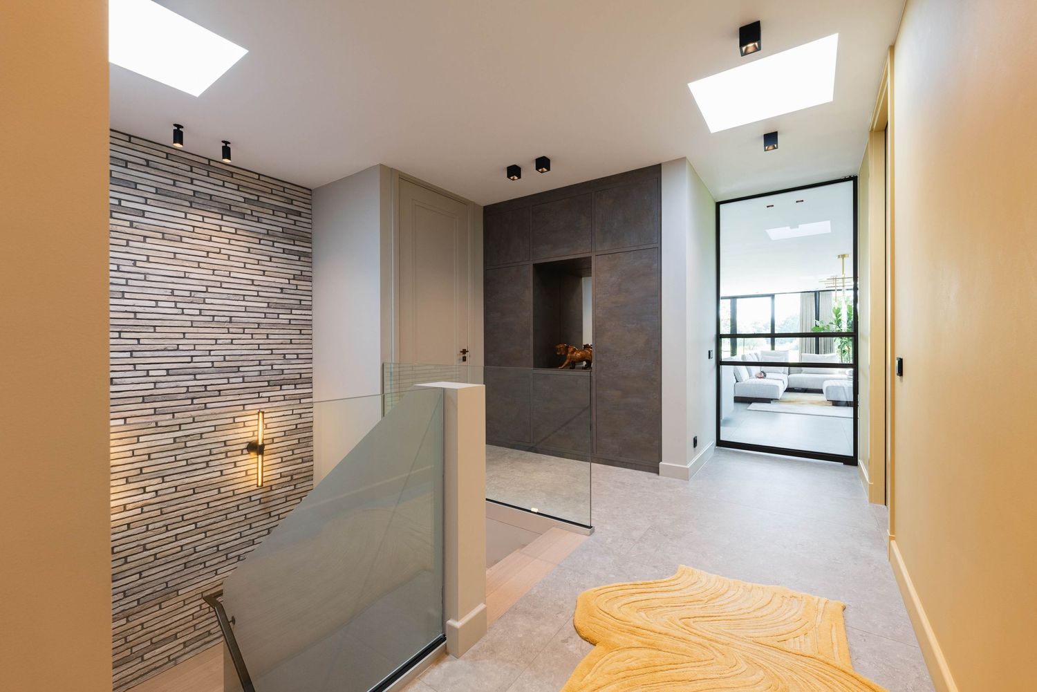 Modern apartment interior with exposed brick walls, skylights, and minimalist white decor features sleek lighting fixtures.