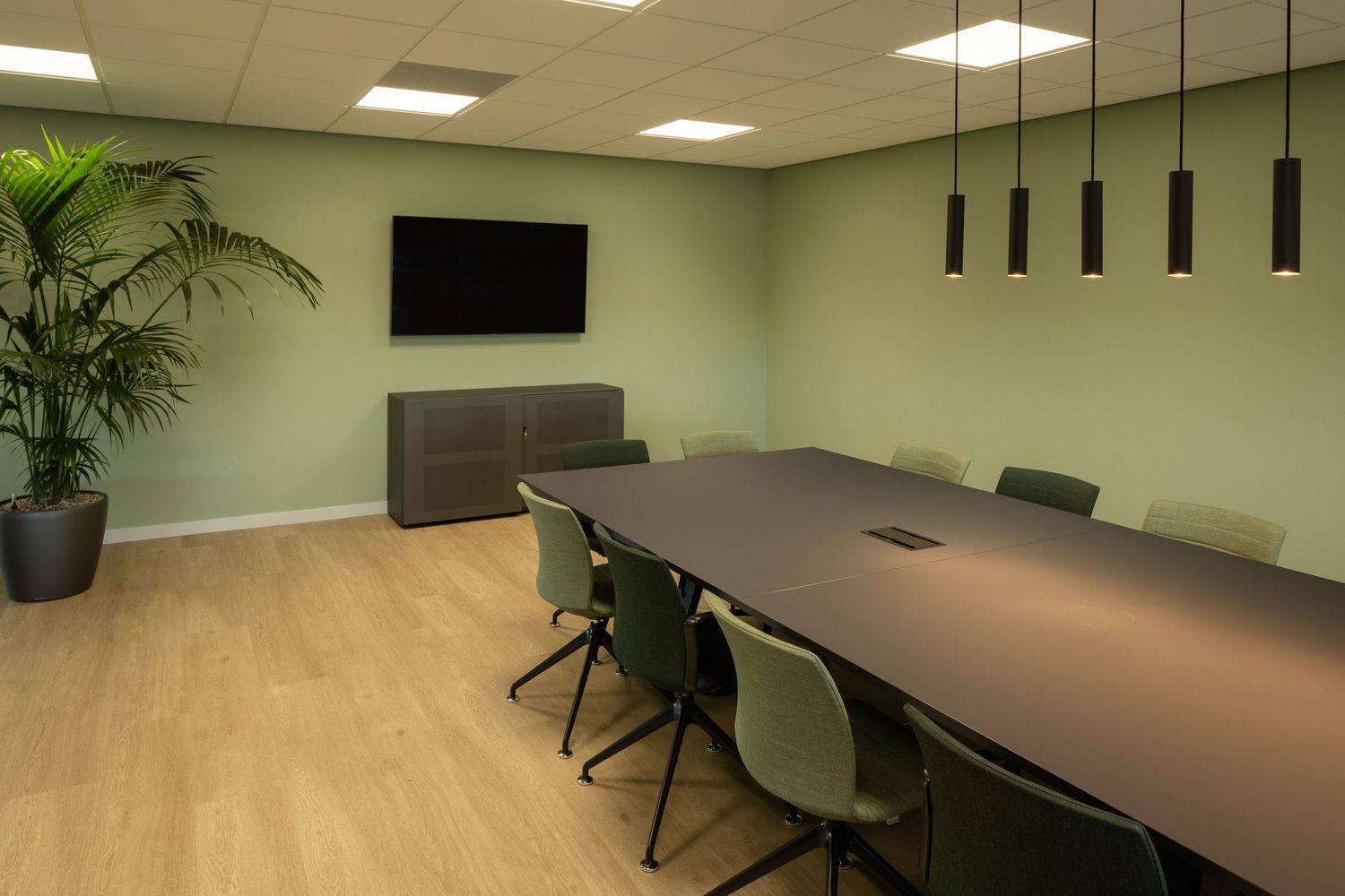 Modern office interior with long conference table, pendant lights, potted plants and mint green walls.