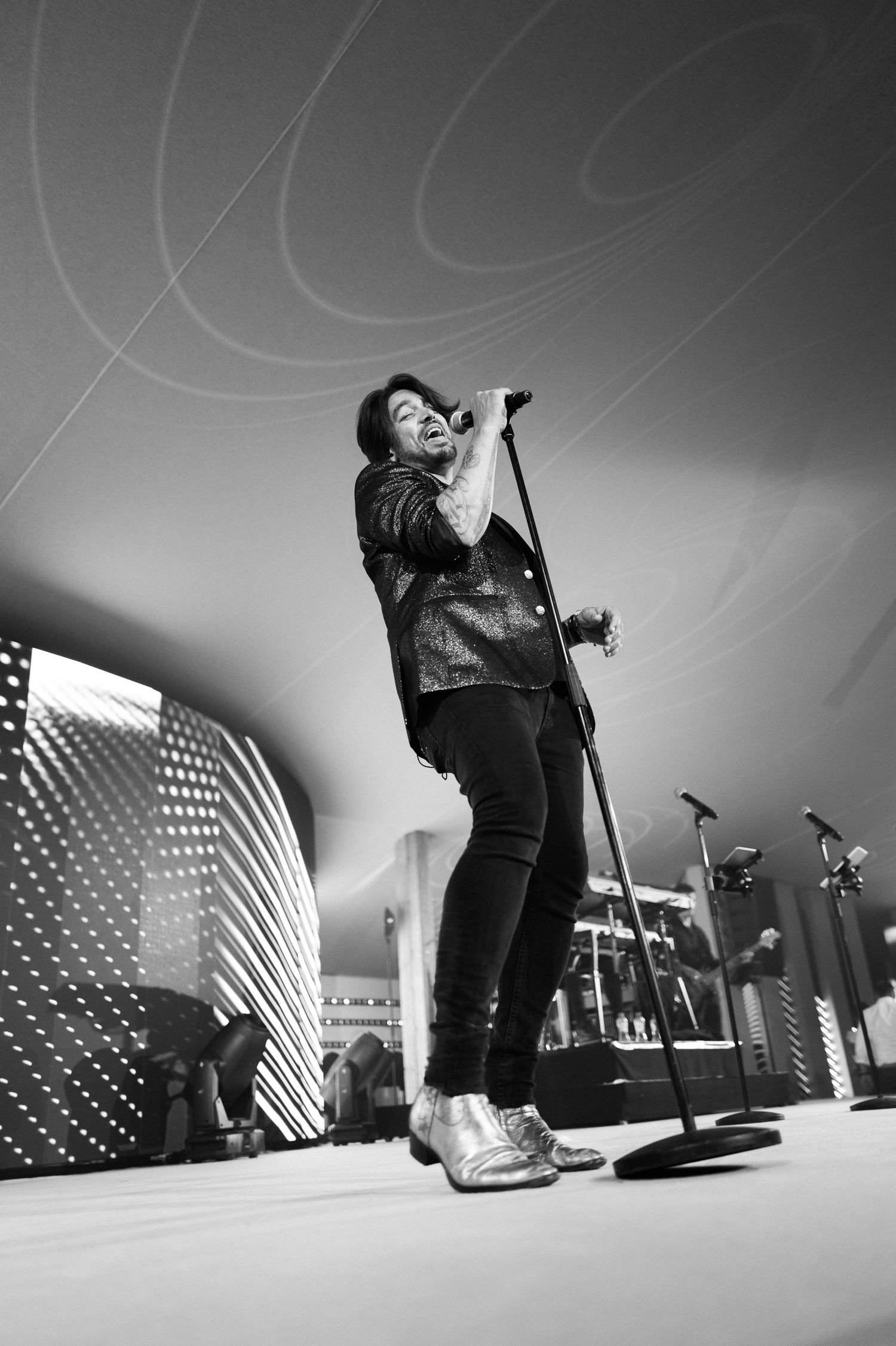 Black and white concert photo of a performer singing on stage with dramatic lighting and curved backdrop.
