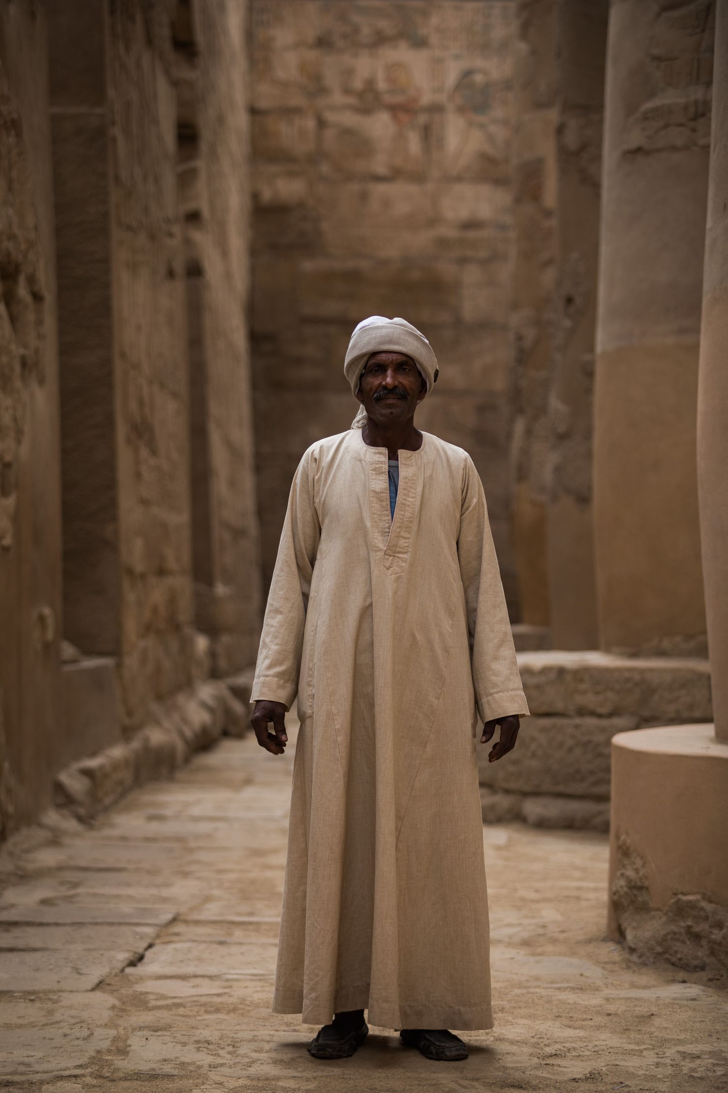 Figure in traditional white robe standing in ancient stone corridor.
