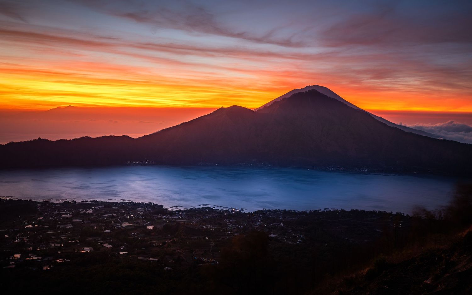 Dramatic sunset silhouette of mountain peaks with orange and purple sky.
