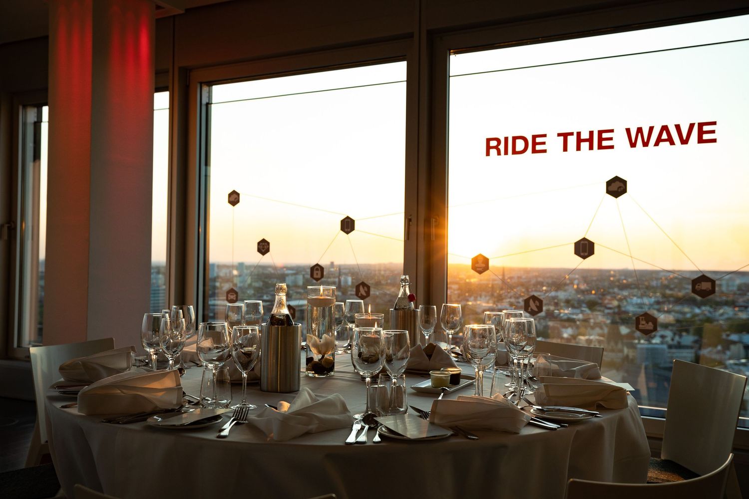 Elegant dining tables set against large windows overlooking a scenic ocean view at sunset.