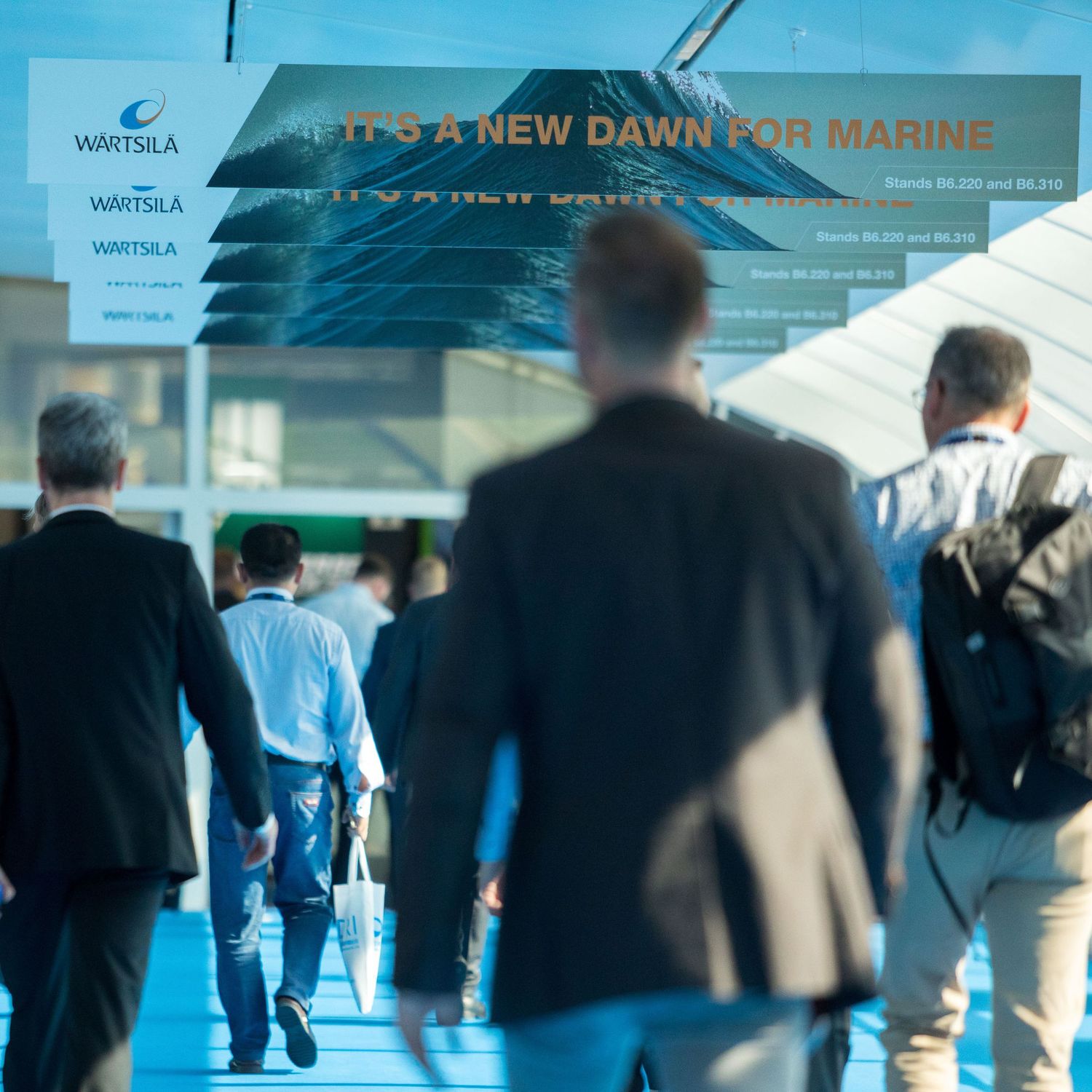 Business professionals gather at a corporate event in a modern blue-lit exhibition space.