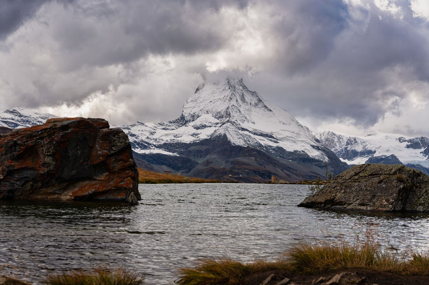 Dramatic cloudy skies over mountain peaks with snow-covered slopes and rocky outcrops.