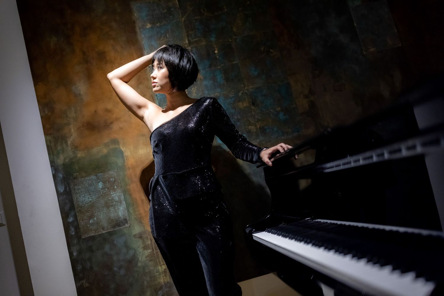 A pianist in black attire performs expressively at a grand piano in a dimly lit concert hall.
