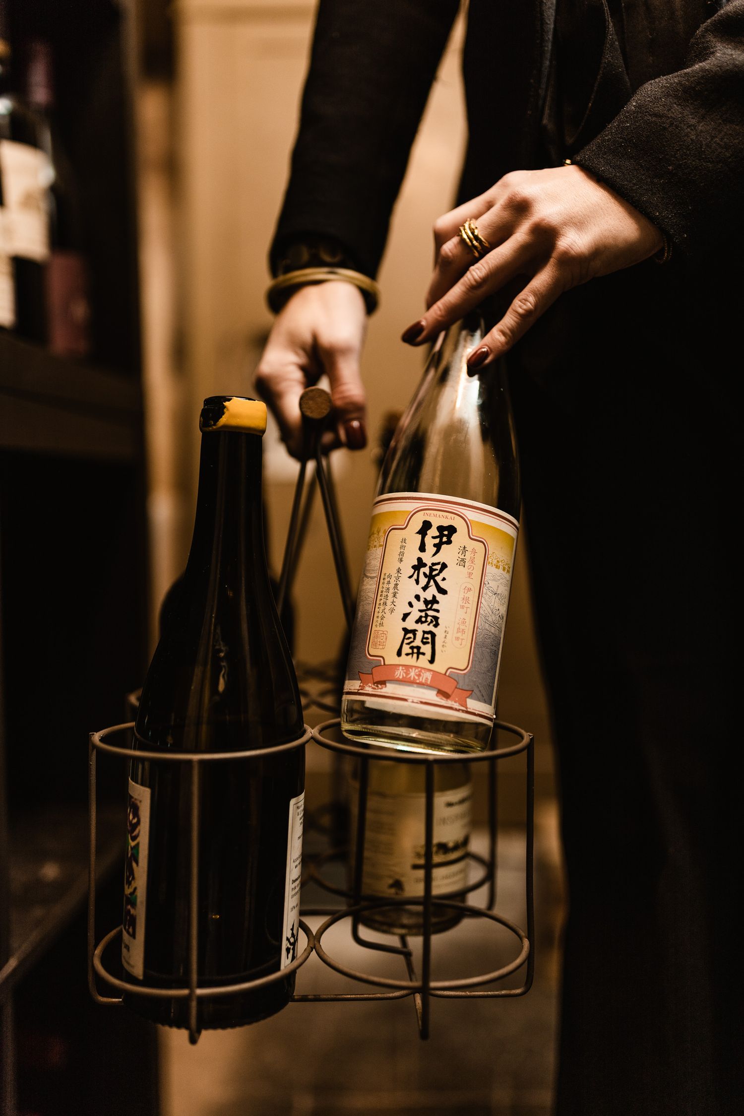 Japanese sake bottles with traditional labels are arranged in metal holders against a warm-toned background.