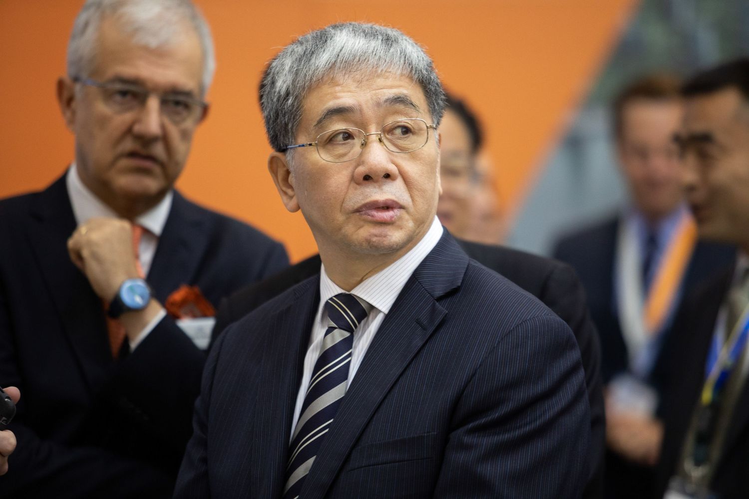 Business executive in glasses and striped tie at professional conference with orange wall background.