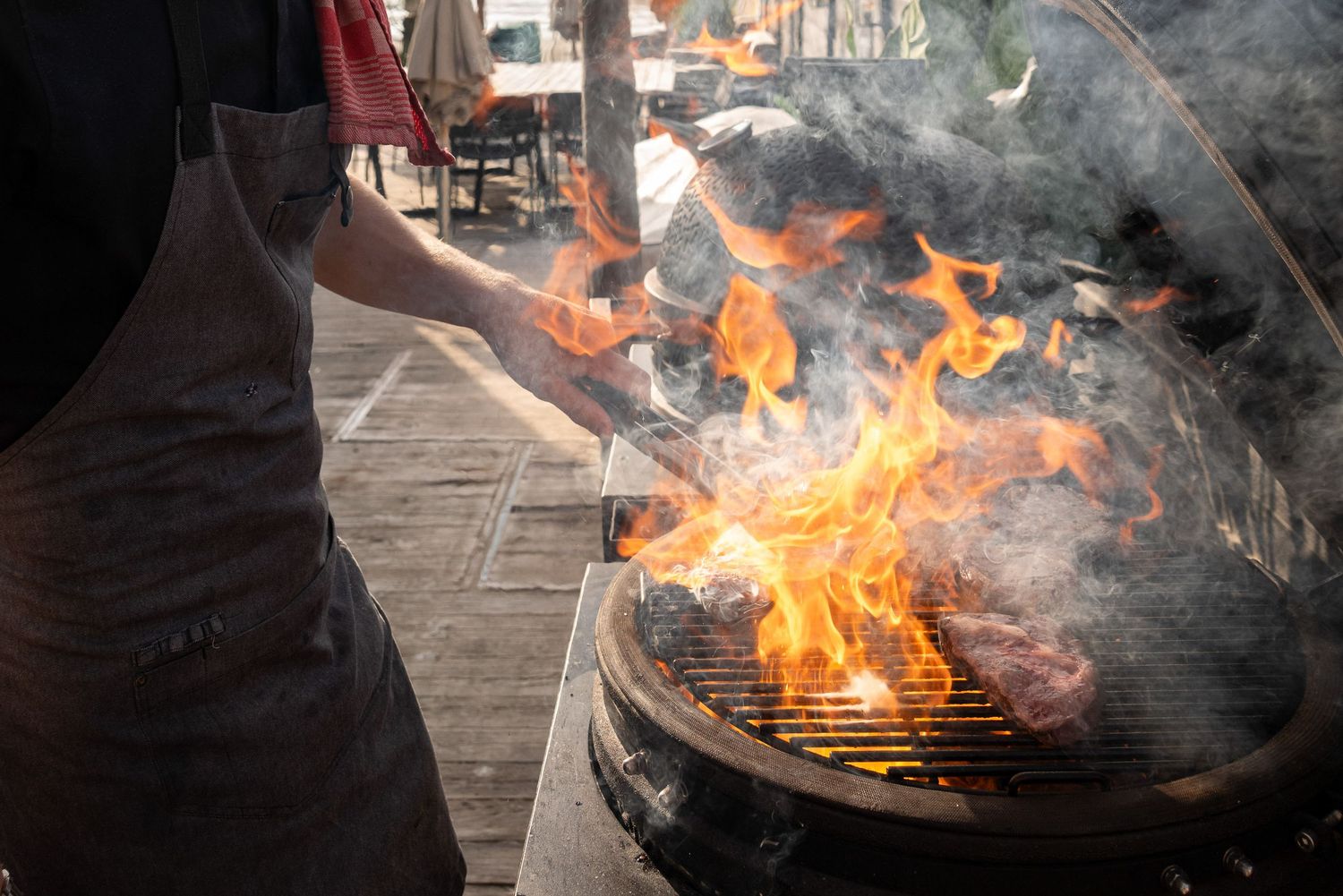 Flames and smoke rising from a large outdoor grill during food preparation.