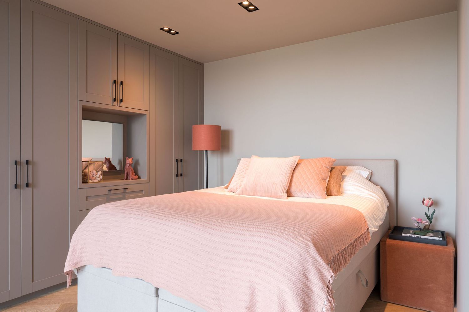 Modern bedroom interior with gray built-in cabinets, pink bedding, and warm lighting creating a cozy atmosphere.