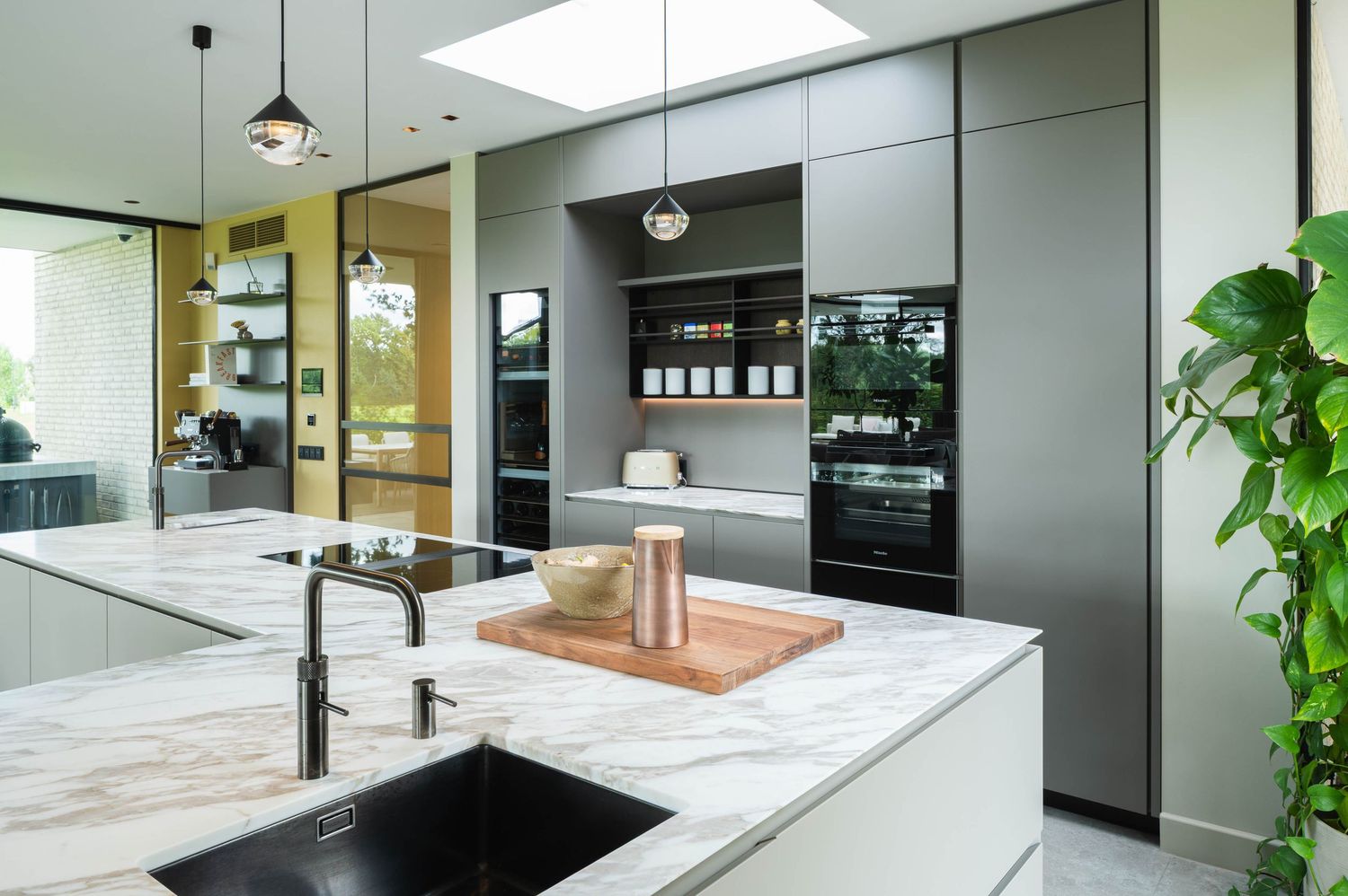 Modern luxury kitchen with marble countertops, black appliances, and pendant lighting features sleek gray cabinetry.