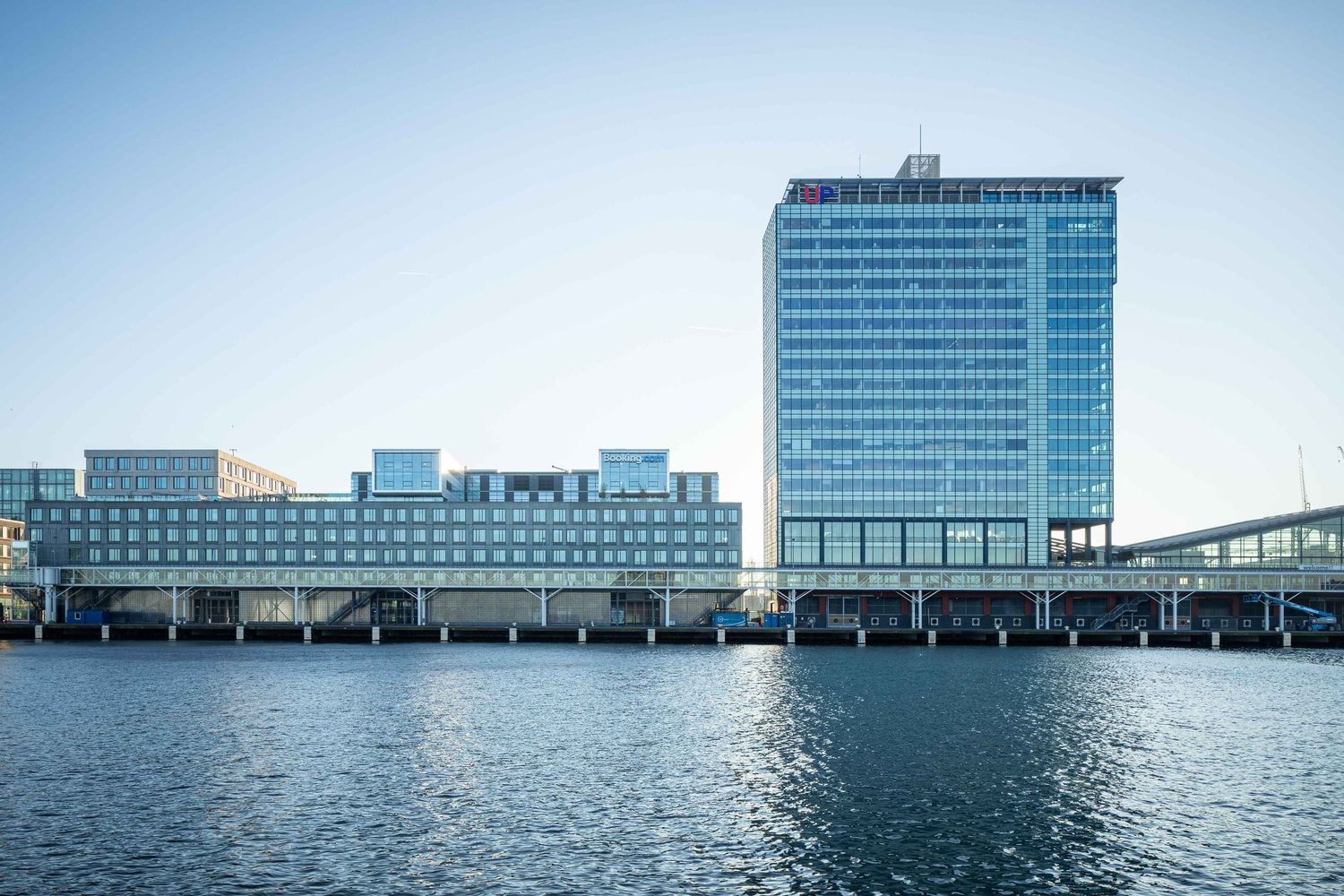 Modern office buildings with glass facades overlooking a calm waterfront in an urban harbor setting.