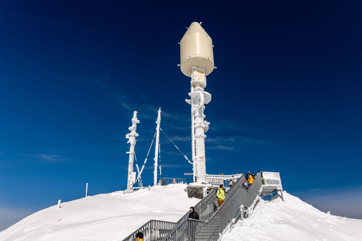Snow-covered meteorological station with communication equipment on alpine mountain peak.
