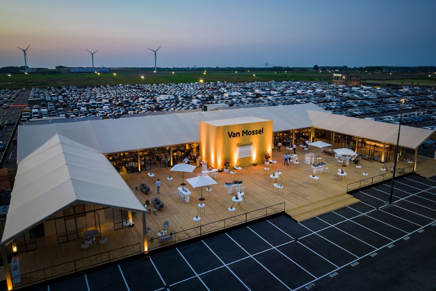 Aerial view of a massive parking lot with wind turbines in the background during sunset.