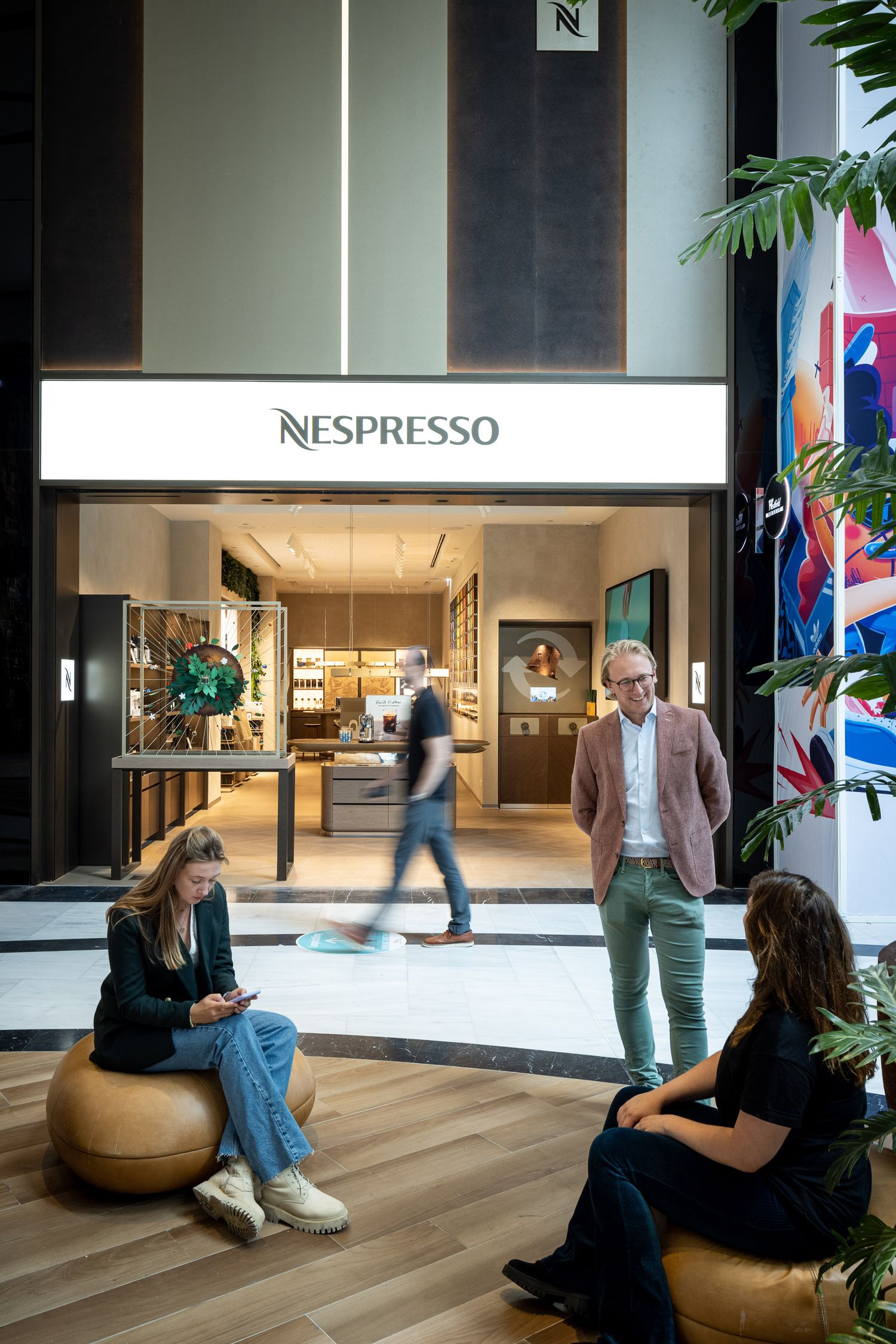 Modern retail space with people relaxing on lounge furniture near a Nespresso storefront.
