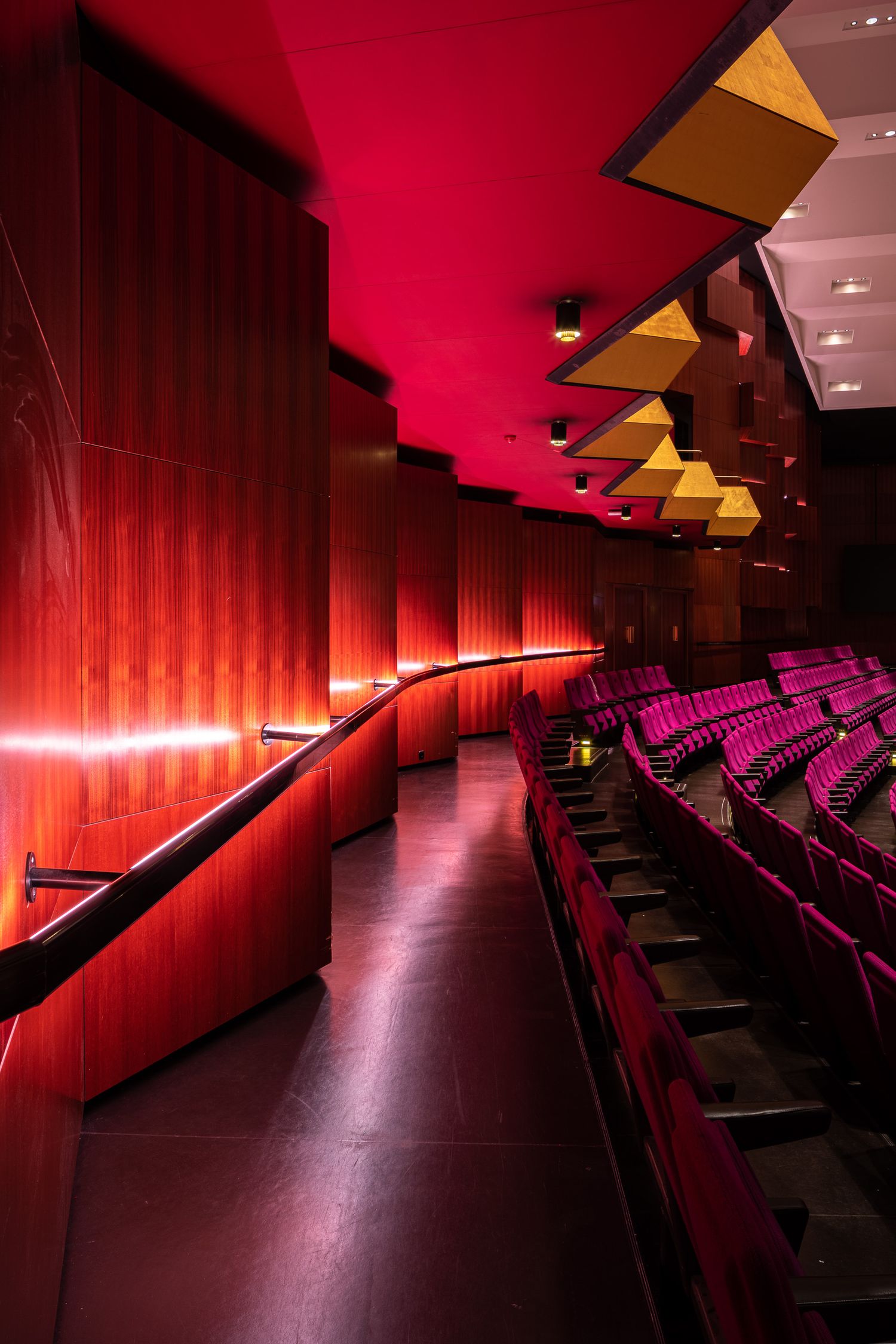 Red-lit theater auditorium with tiered seating and dramatic lighting creates a moody cinematic atmosphere.
