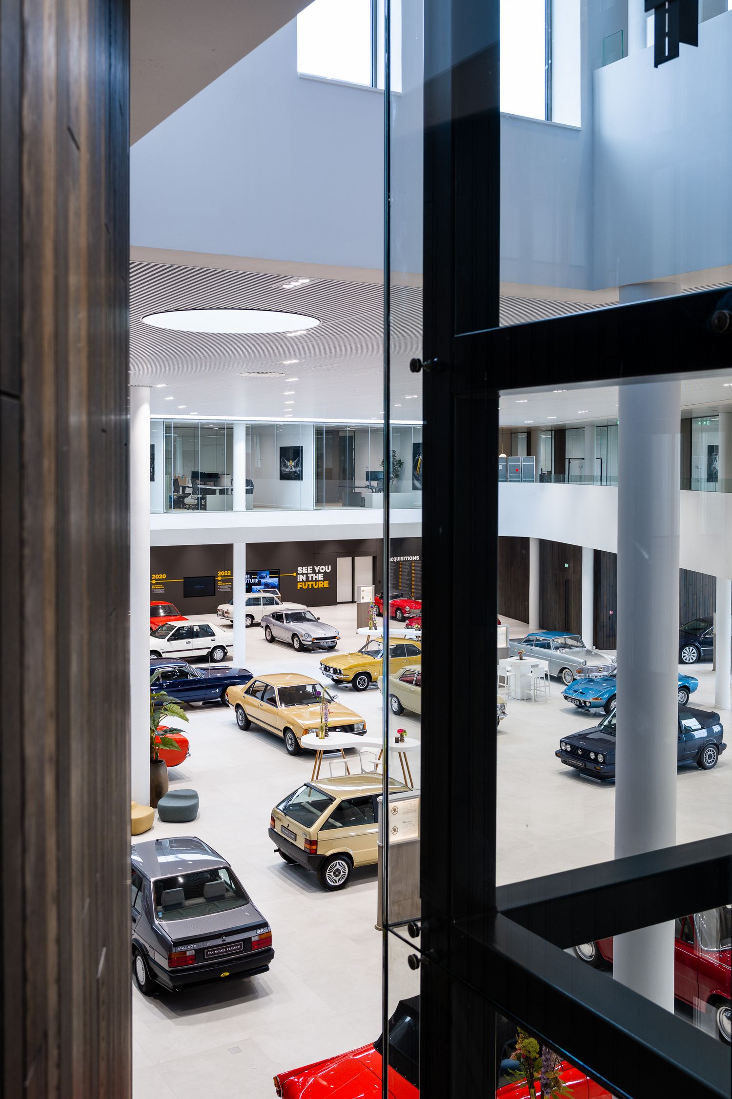 Modern car showroom interior with classic and vintage vehicles on display across multiple levels viewed through glass panels.