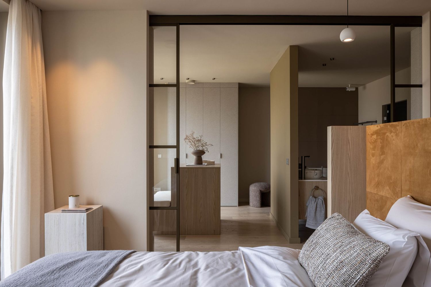 Modern bedroom interior with sliding glass doors leading to an ensuite bathroom and neutral color scheme.