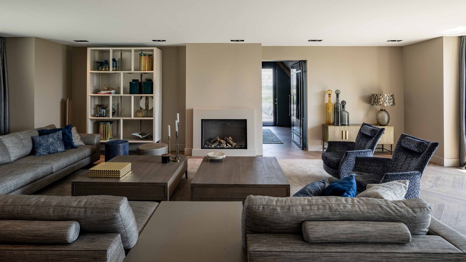 Modern living room with built-in fireplace, gray sectional sofa, blue accent chairs and custom shelving unit.