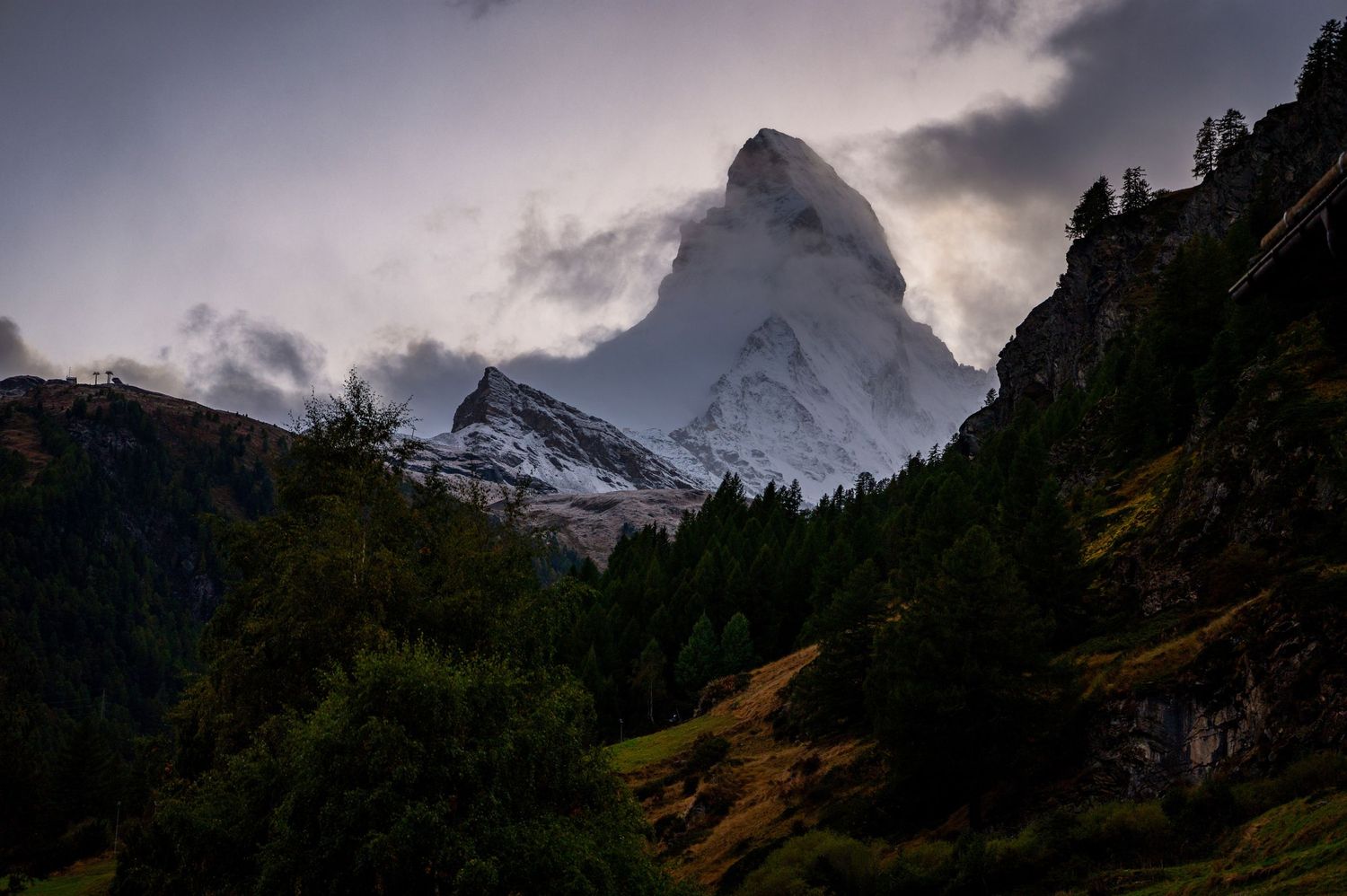 Dramatic mountain peaks silhouetted against cloudy sky during sunset in alpine landscape.