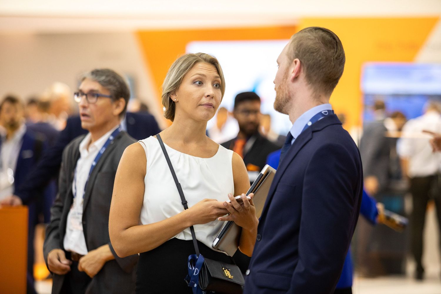 People gather at a business networking event in a bright conference space with orange accents.