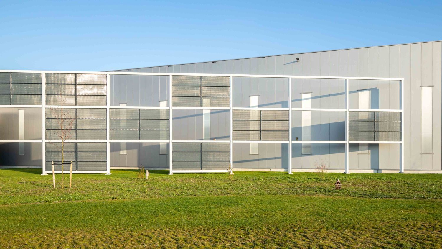 Panoramic view of a modern industrial building complex with glass walls against a blue sky and green landscape.