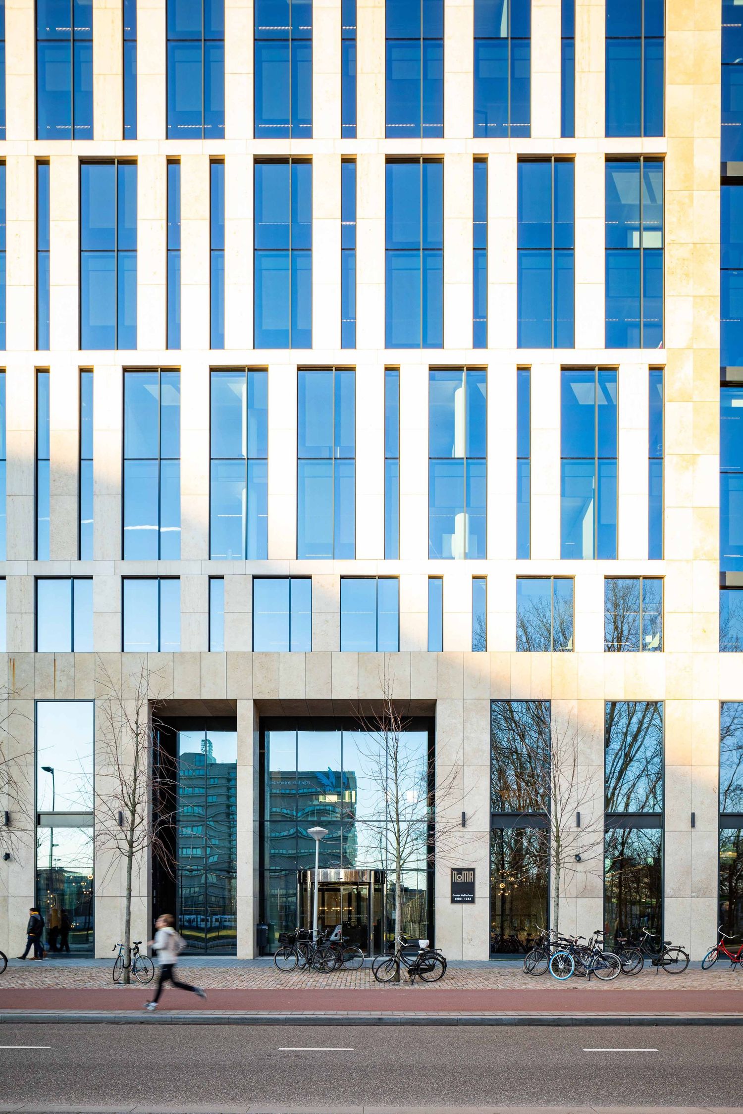 Modern office building exterior with blue glass windows and white facade elements on a sunny day.