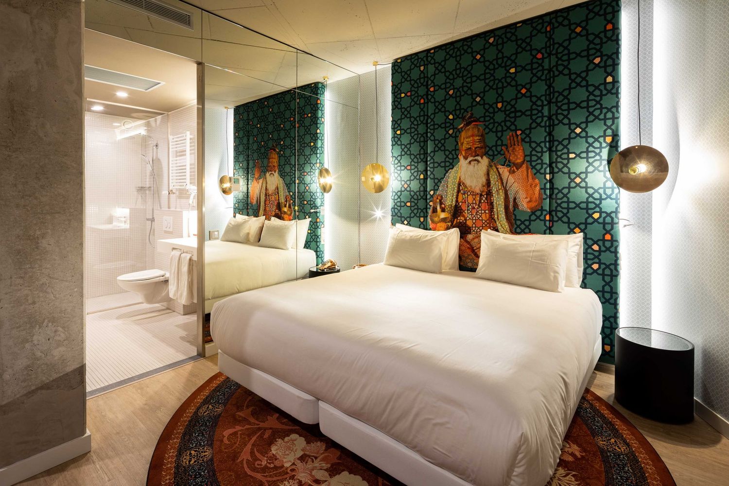 A modern hotel bedroom suite with teal wallpaper, pendant lighting, and white bedding showcases contemporary design elements.
