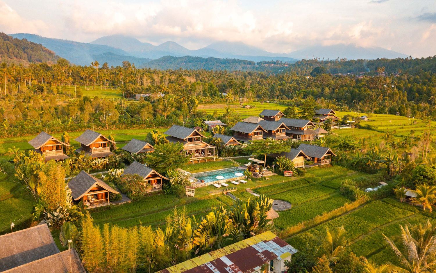 Aerial panorama of mountain resort village with wooden cabins scattered across golden meadows.