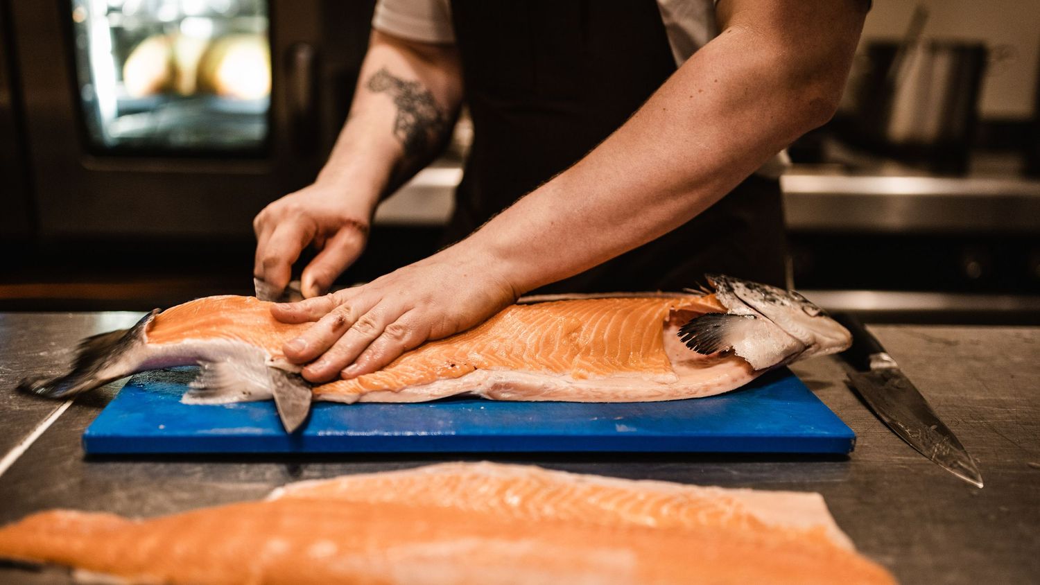 Chef preparing raw salmon fillets on a wooden cutting board in a professional kitchen.