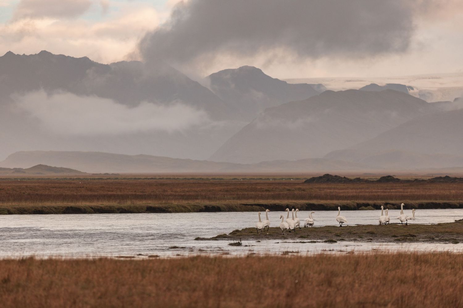 Dramatic panoramic view of a rugged mountain landscape with moody clouds and misty peaks at sunset.