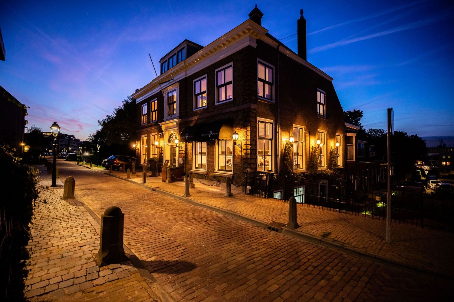 Charming brick building illuminated at dusk with warm glowing windows on a cobblestone street corner in historic town setting.